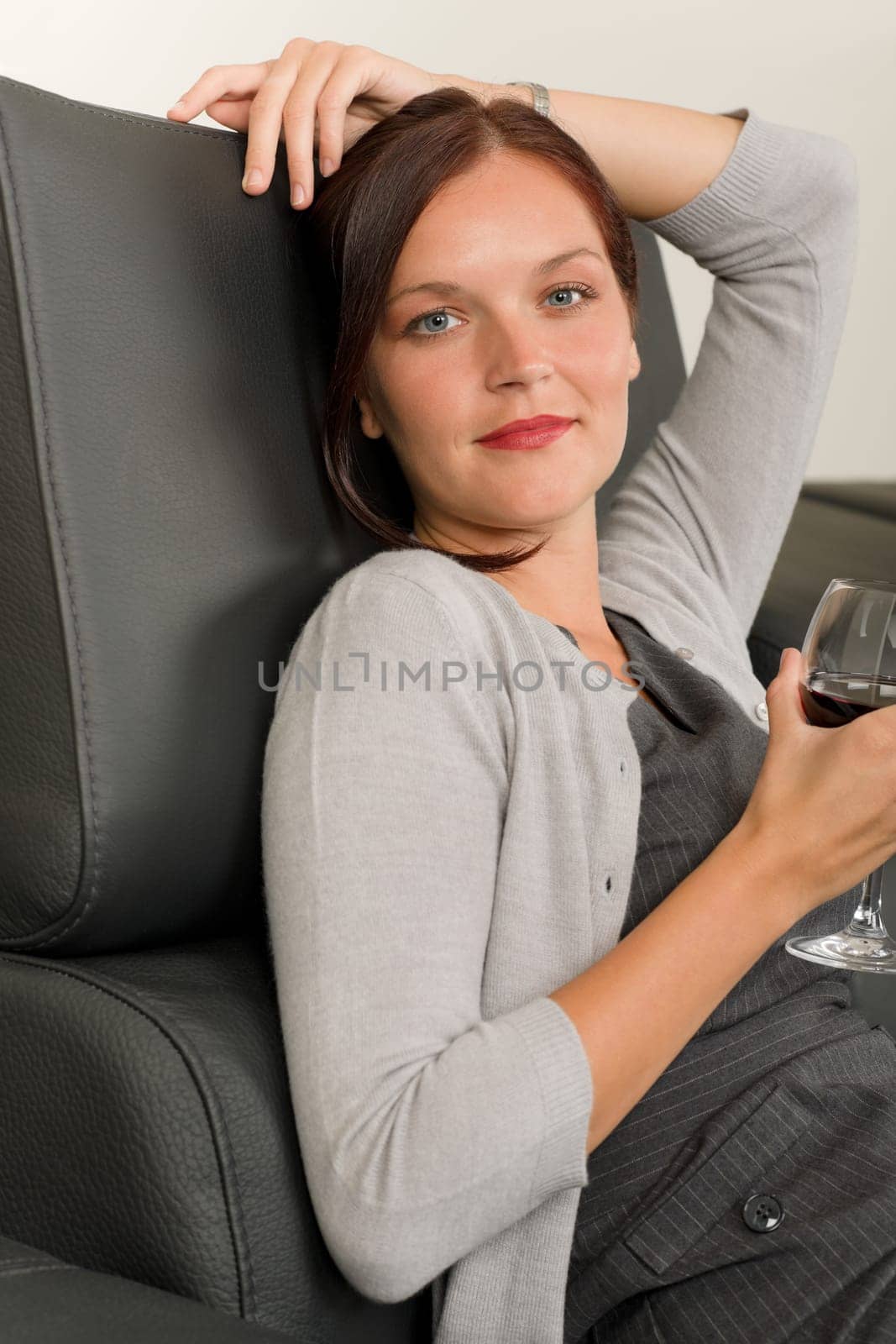 Elegant businesswoman sitting on leather sofa drink glass red wine