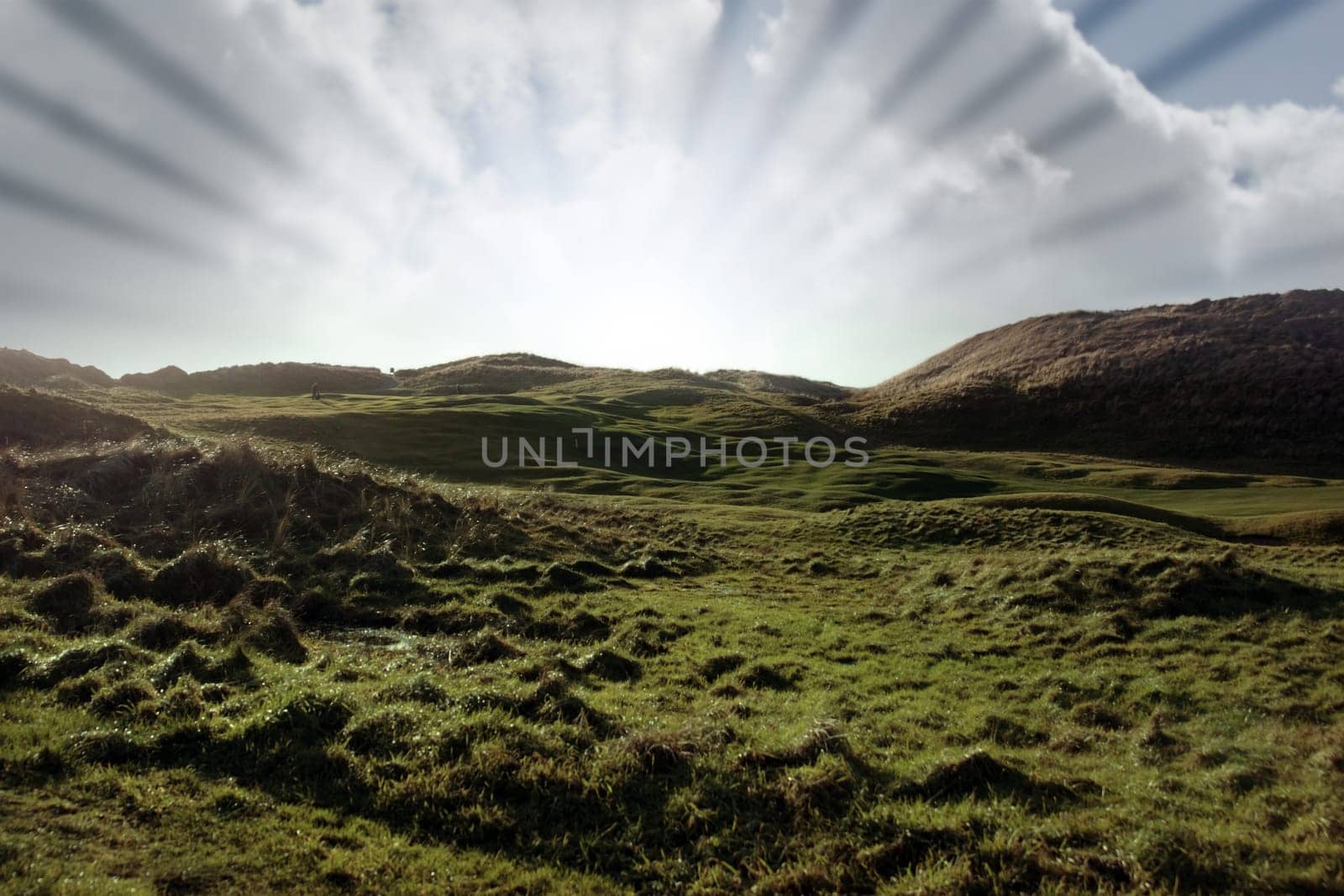 golfers playering and on a hole on a links golf course in ireland with sun rays in background