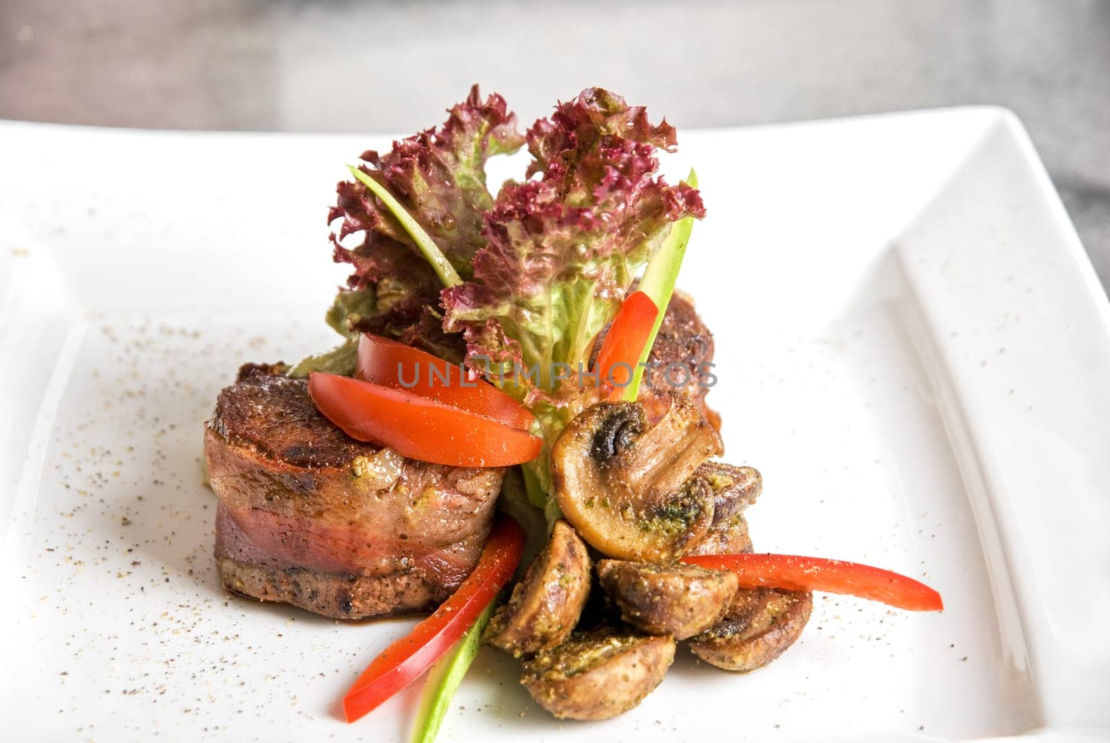 Tasty beef steak grilled in a cast-iron ribbed fry pan with bacon decorated with vegetables and roasted mushrooms