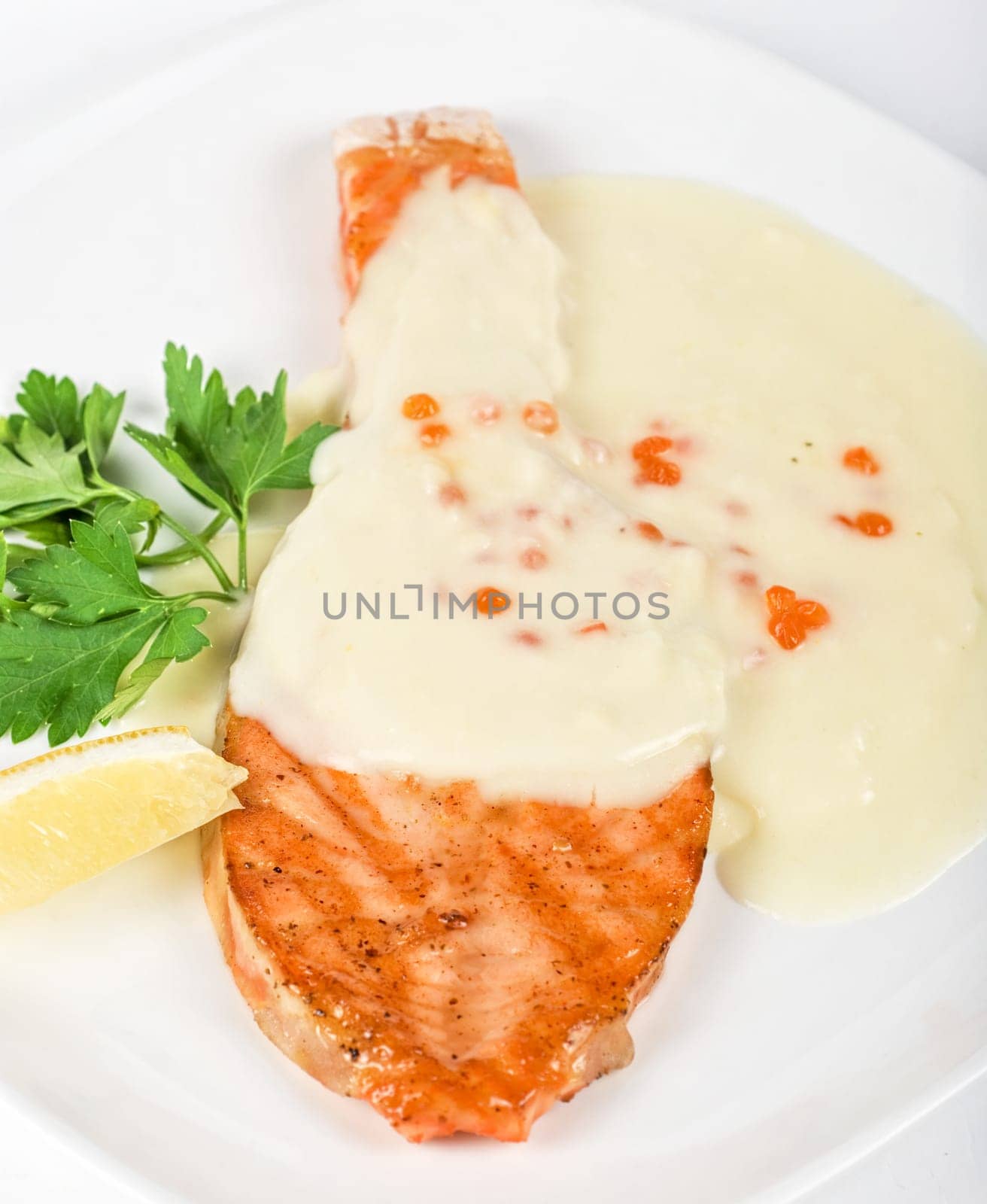 Grilled salmon steak with cheese sauce, greens, lemon and red caviar