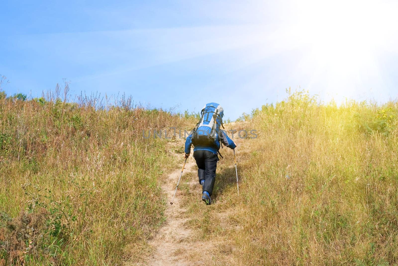 Hiker with rucksack up-hill at summer sunny day