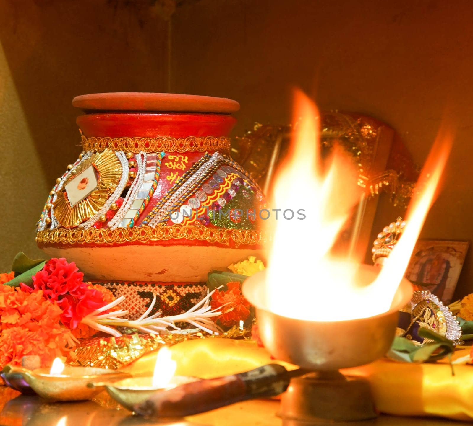square format portrait of Hindu Hinduism religion religious worship of Navratri event home with puja decorated clay pot matti, flowers a ghee diwa candle and pictures of hindu idols crop margin