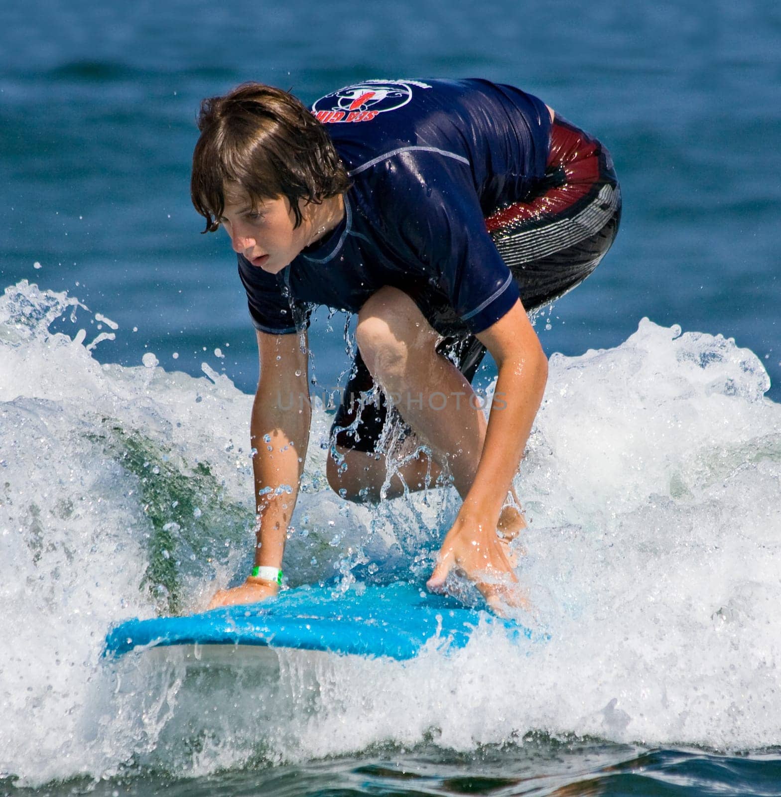 A teenager surfing. The boy is just beginning to stand up on the surfboard.