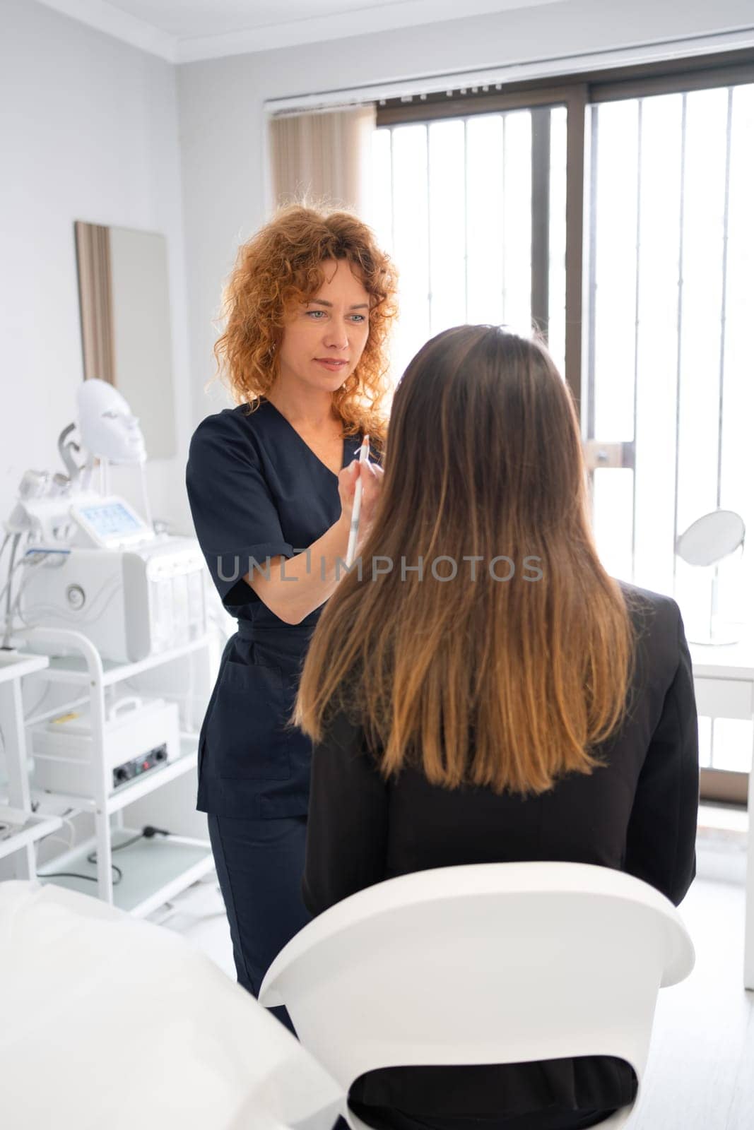 Female dermatologist examining anonymous client's skin in beauty spa salon. Beautiful cosmetologist woman is looking at customer's face while working in clinic