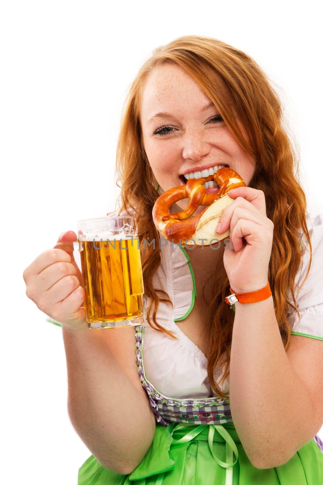 Young redhead woman in dirndl holding beer and eating pretzel on white background