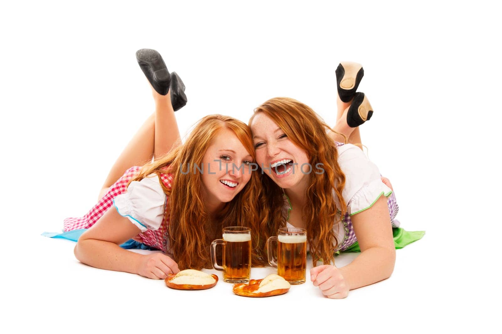 Two happy women in dirndl with beer and pretzels lying on the floor on white background