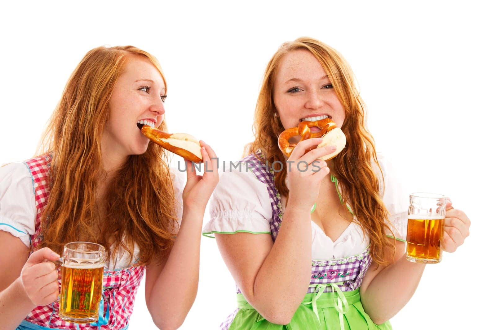 Two women in dirndl with beer eating pretzels on white background