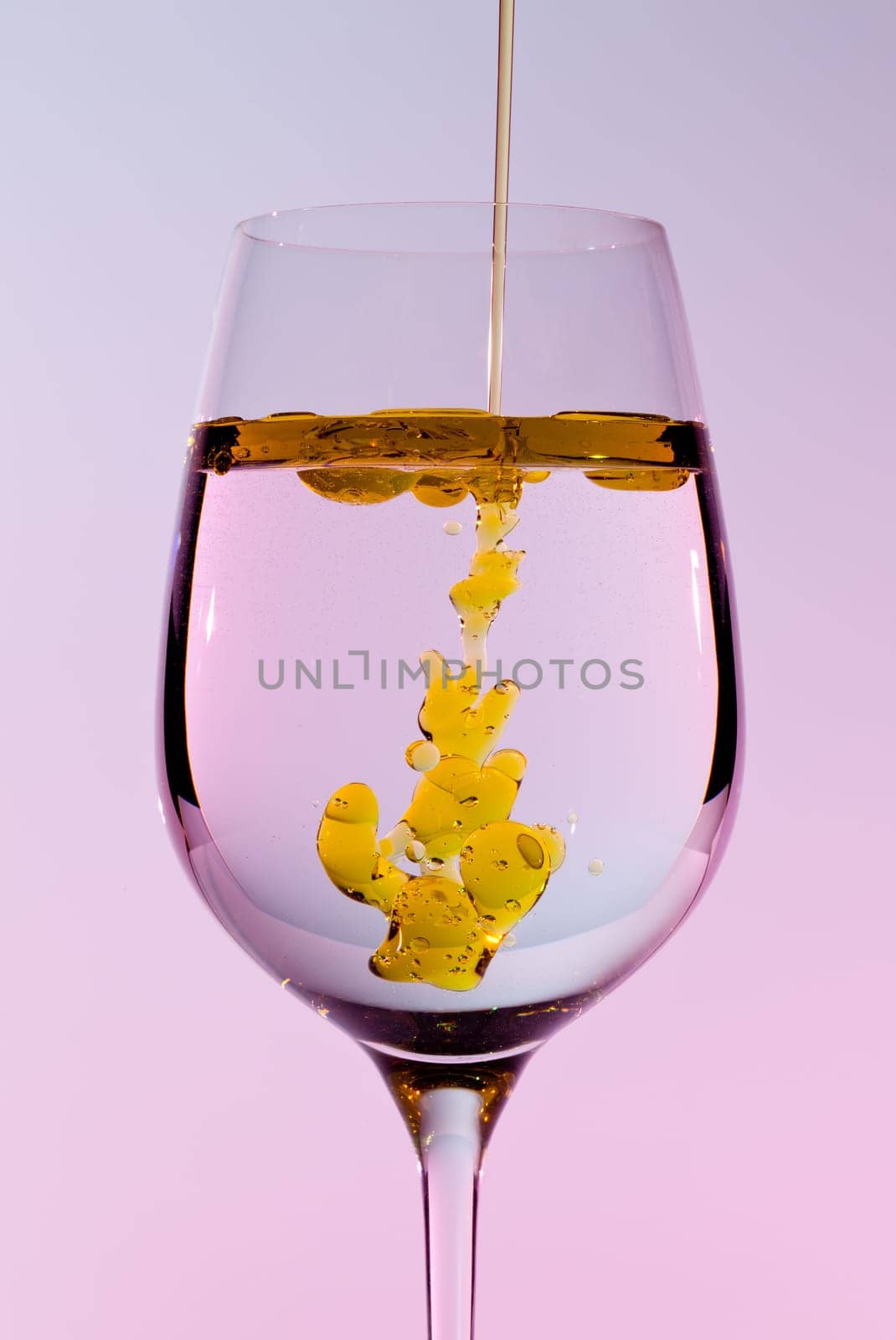 Olive oil being poured into a large wine goblet forming golden bubbles in the liquid