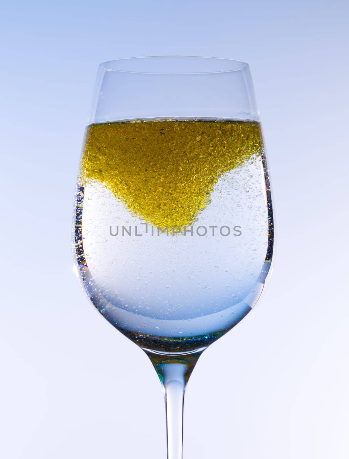 Olive oil being stirred in a large wine goblet forming golden bubbles in the liquid