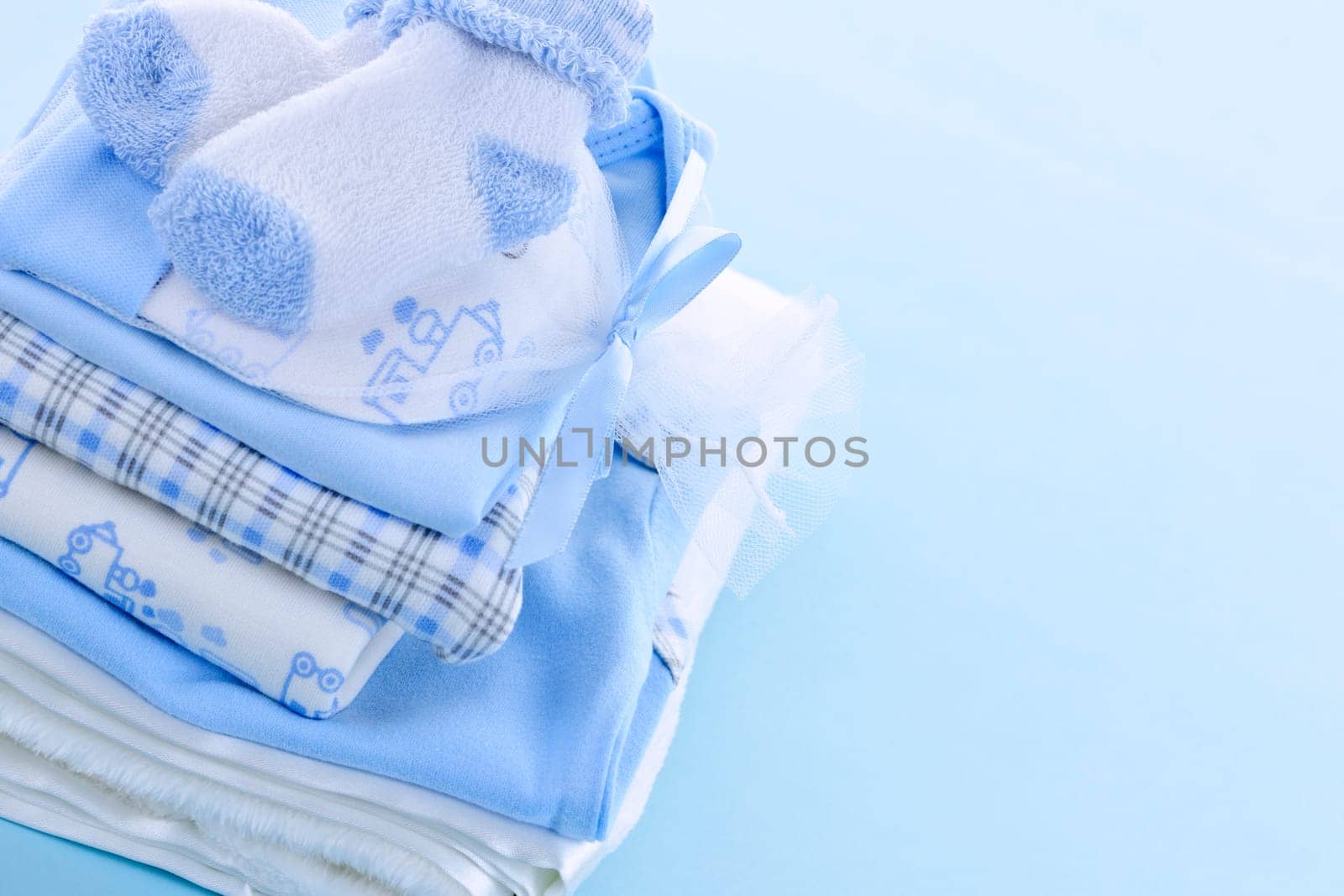 Stack of boy infant clothing for baby shower on blue background