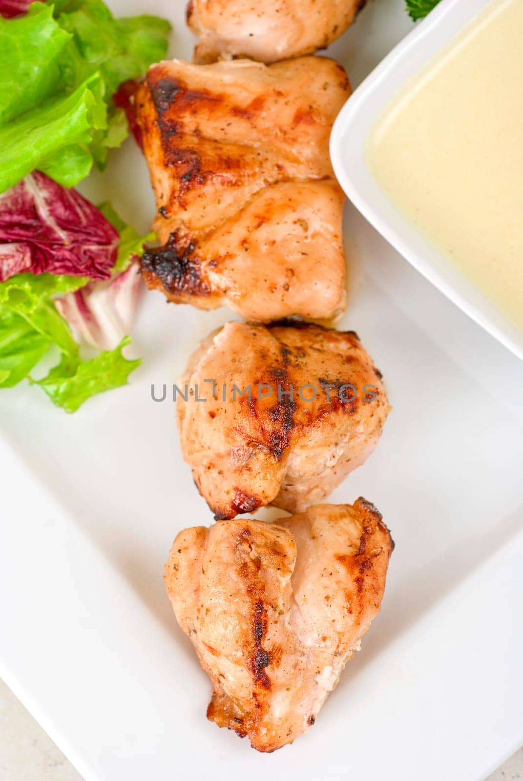 Grilled chicken kebab with sauce and greens on white plate