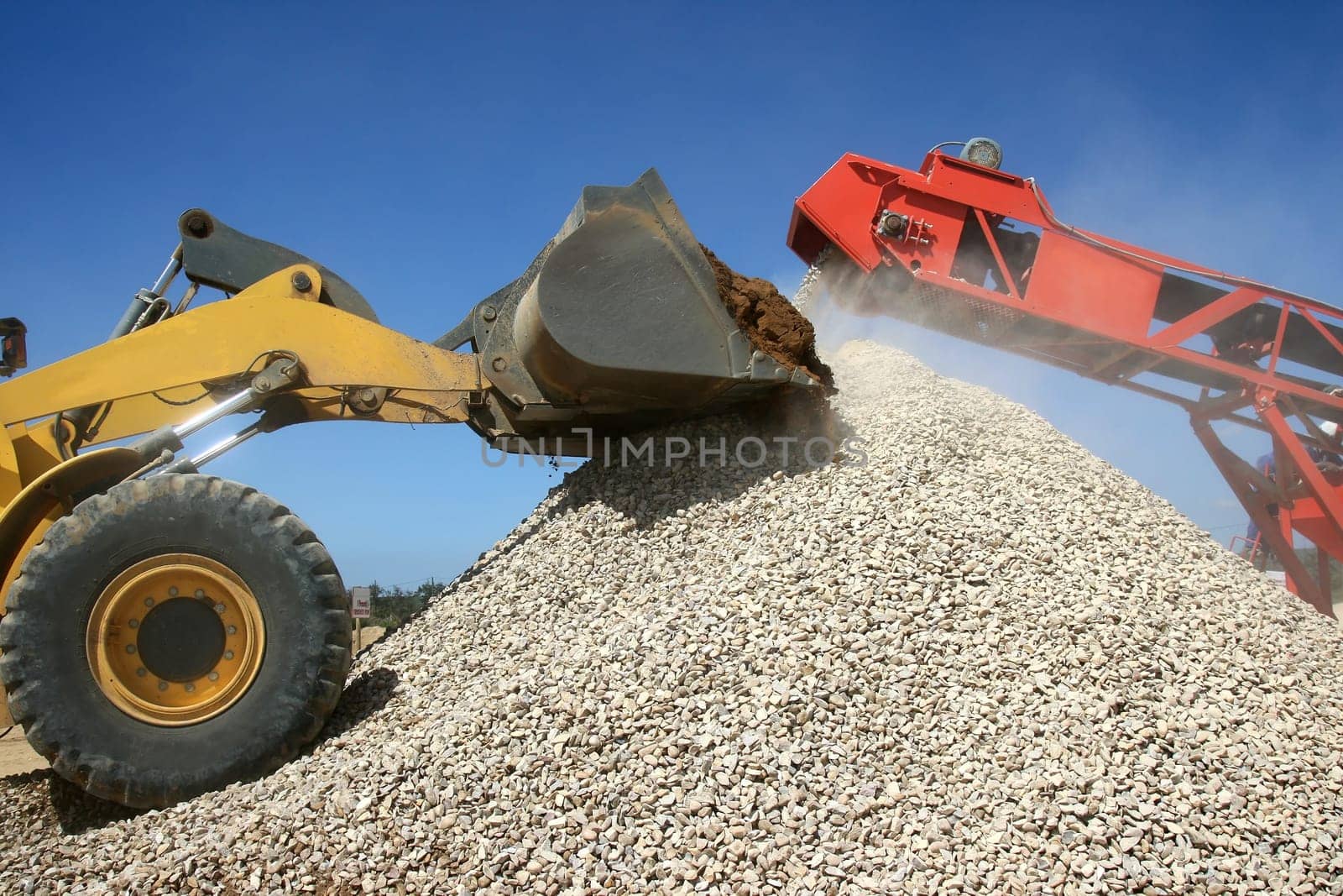 Front end loader and conveyor belt on a pile of graded stone