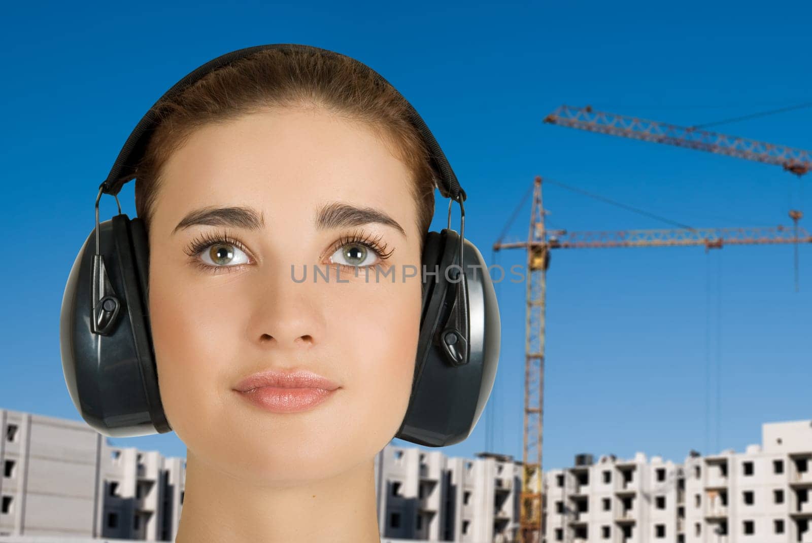 Builder pretty girl at safety earphone on a building background