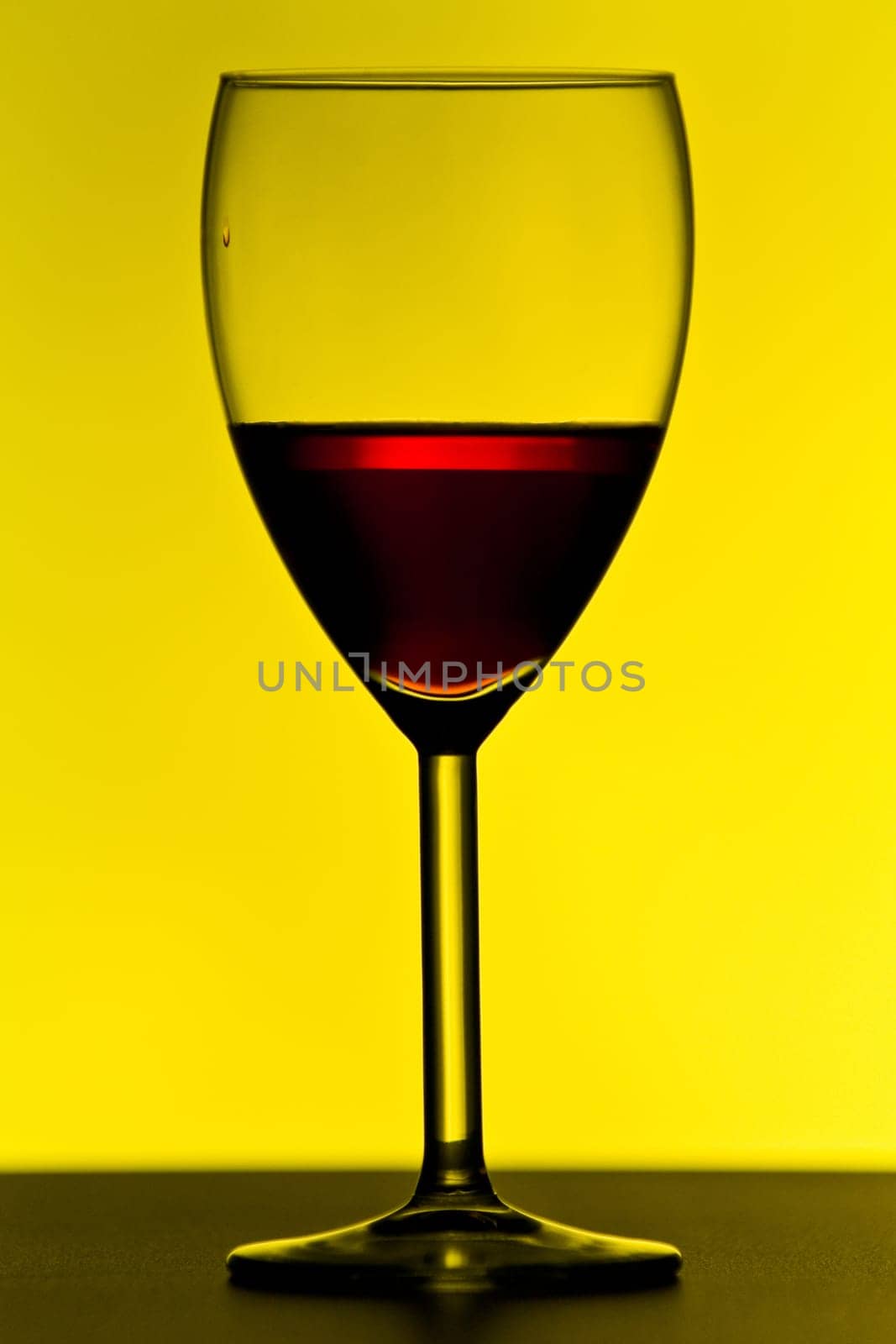 Red wine glass on table with yellow background and strong contrast