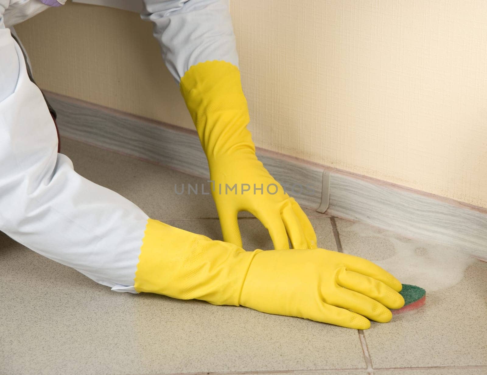 Hands in yellow gloves with sponge, washing floor and plinth