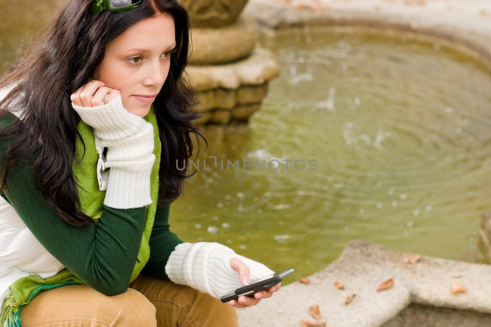 Autumn park young woman dialing phone sitting on fountain