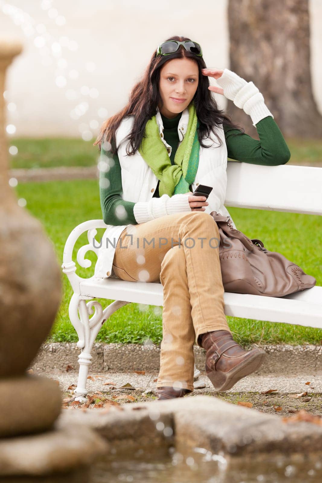 Autumn park young woman dialing phone sitting bench by fountain