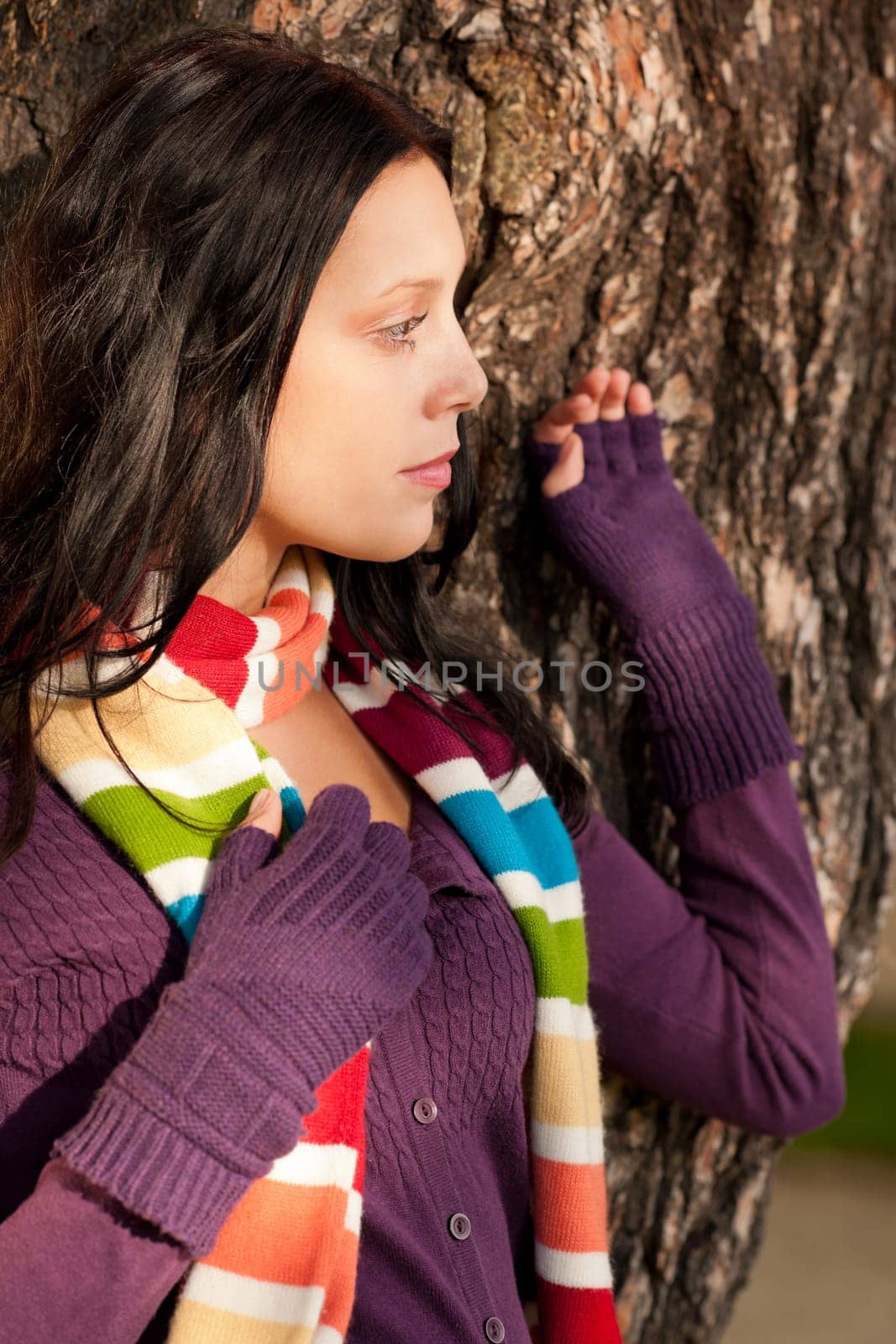 Winter outfit portrait of beautiful female model posing by tree bark