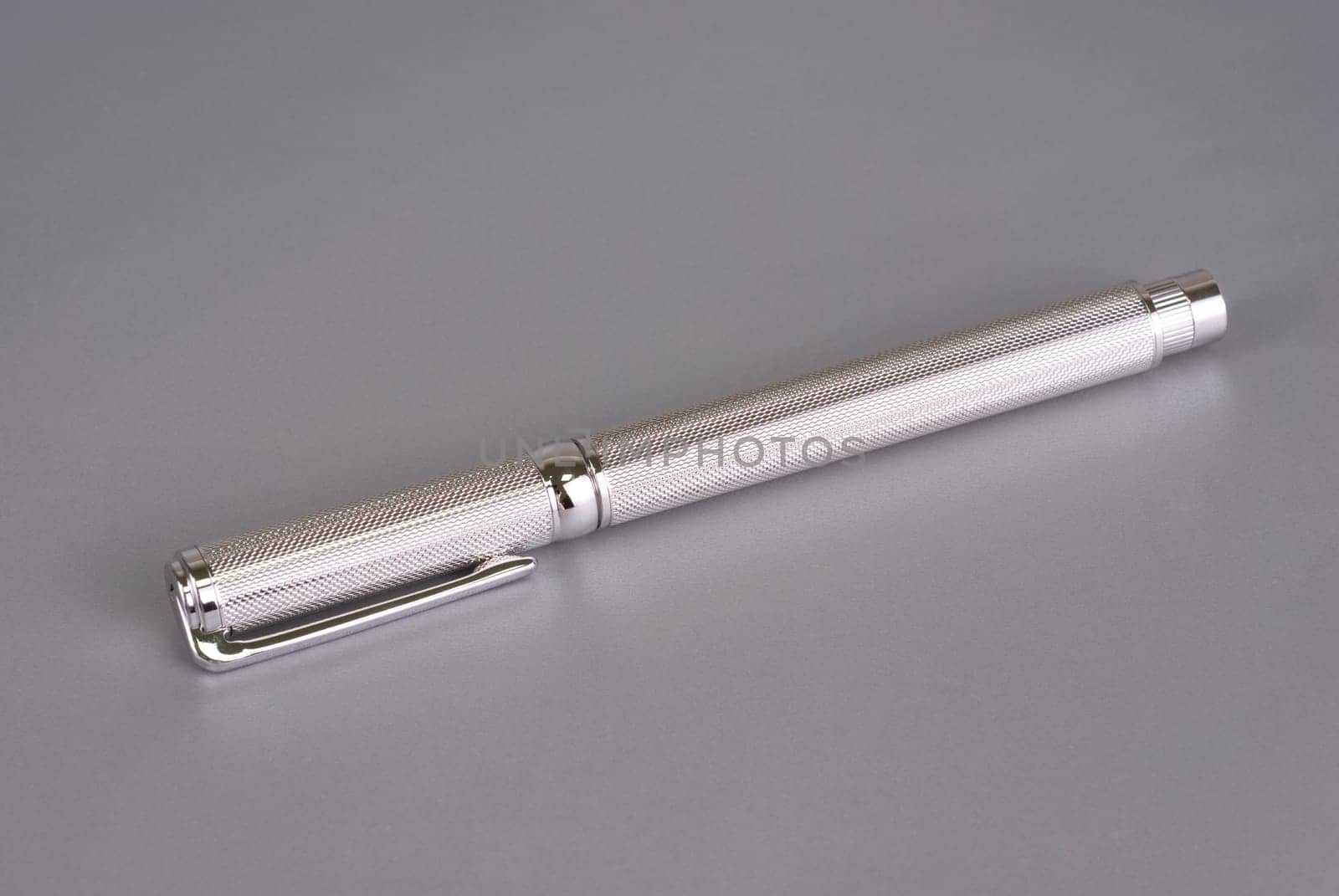 Stylish ballpoint pen of white gold on a grey