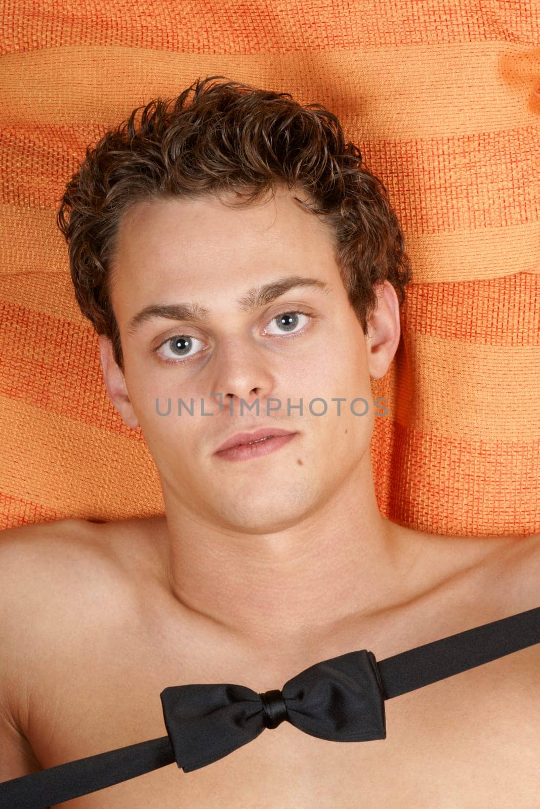 Sexy shirtless young man with bow tie over an orange background