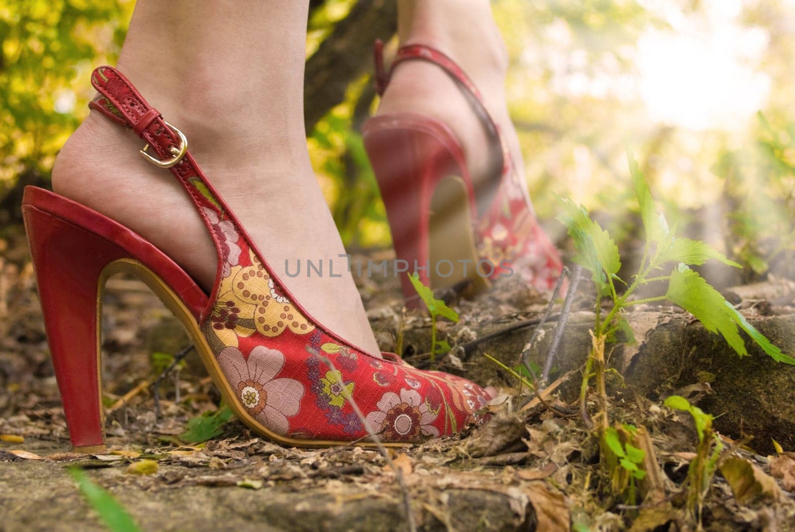 Pair of female feet high-heeld on red shoes. Woman stands on stone staircase. She meets a dawn in the wood.