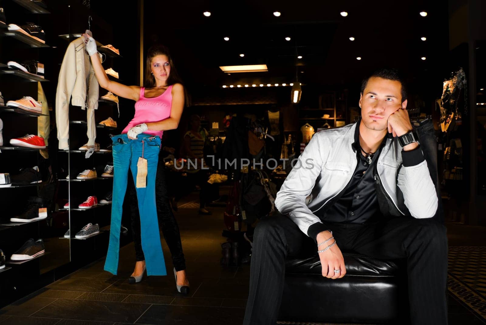 Pair of young adults trying on new clothes in dress storee. The man in fashion suit tired of infinite woman&#039 s clothes. His girl friend shows him different variants of wearings.