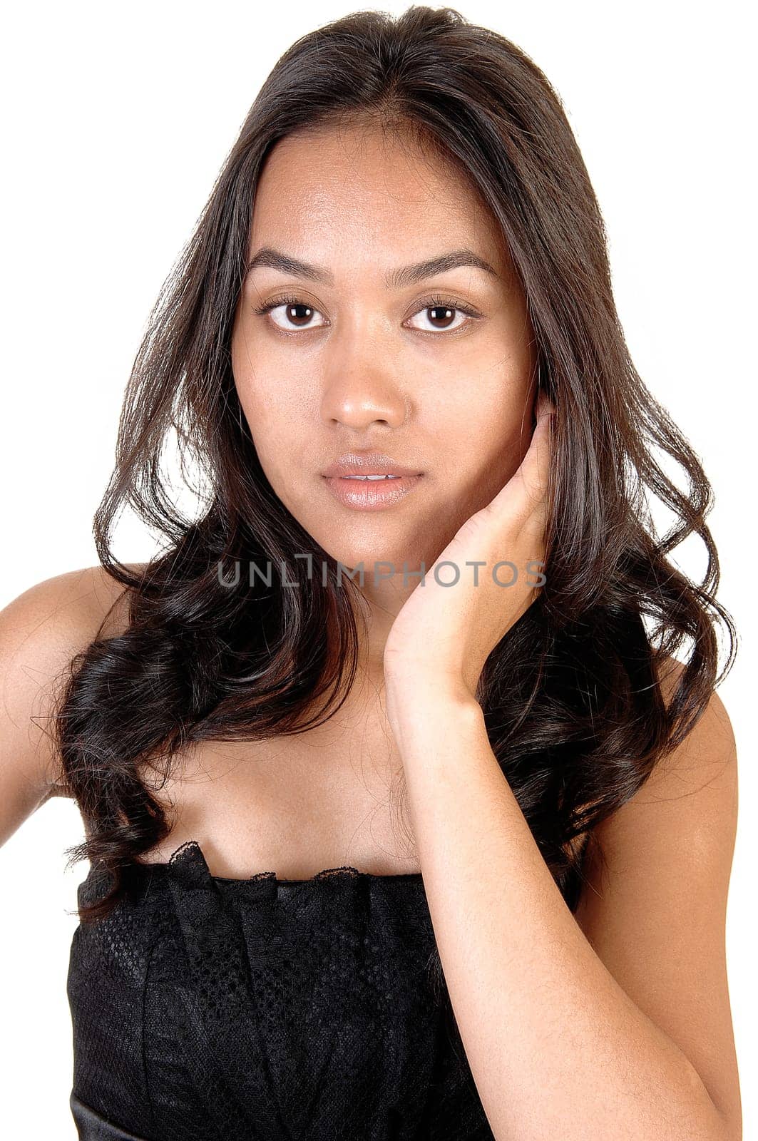 The portrait of a beautiful Asian woman with long curly brunette hair holding one hand on her face, in a black dress over white.