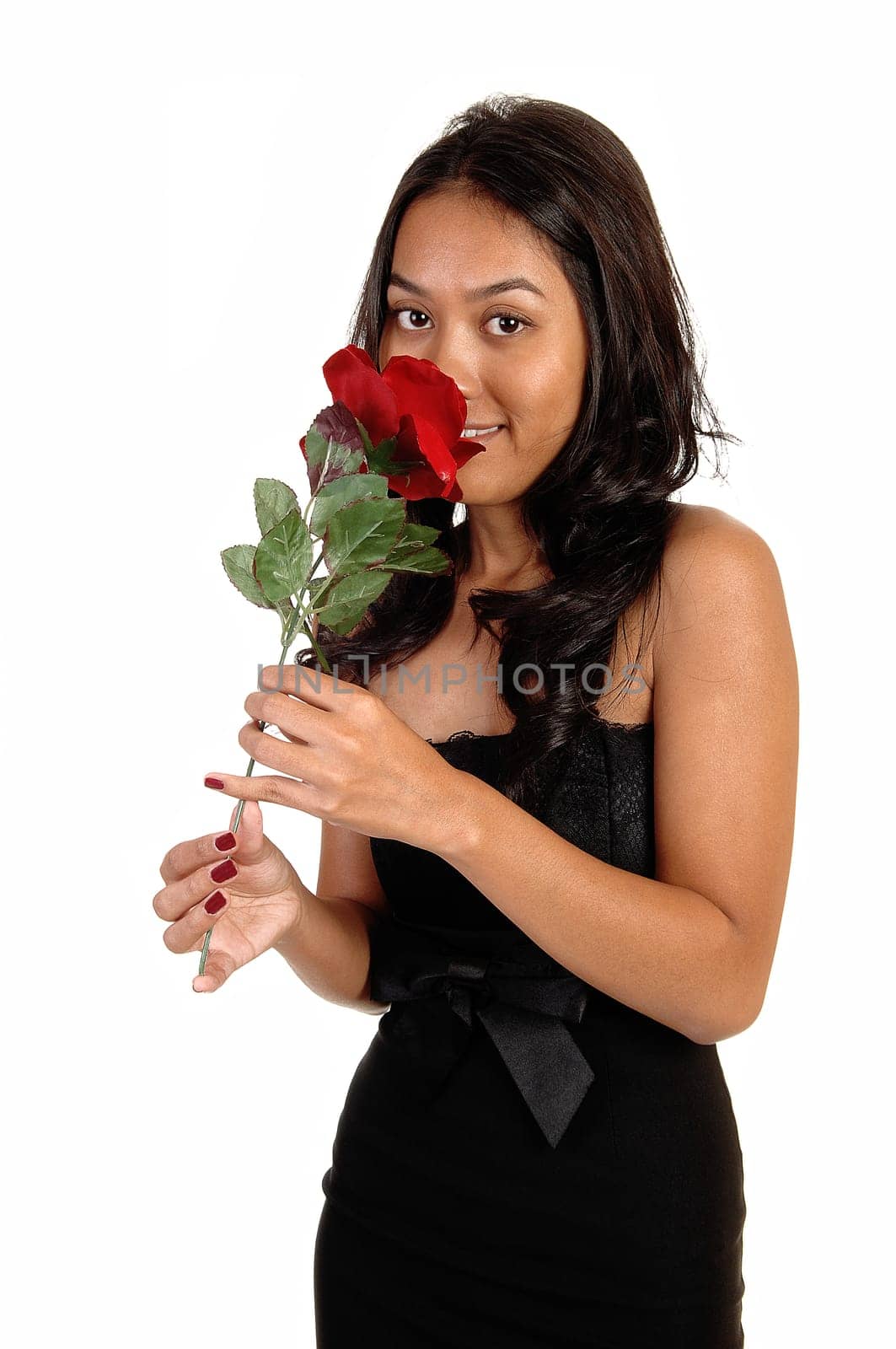 A beautiful Asian woman standing in a black dress, with her long brunette hair, smelling a red rose and smiling, for white background.