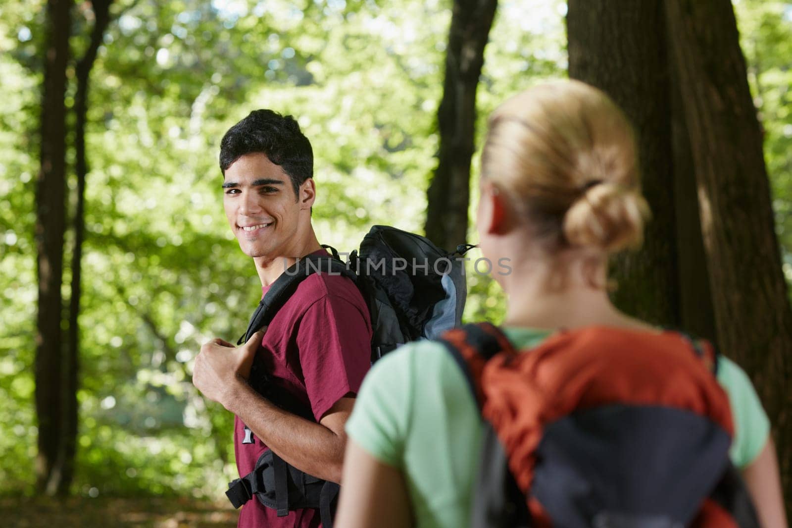young man and woman during hiking excursion, with man looking over shoulders. Horizontal shape, rear view, waist up