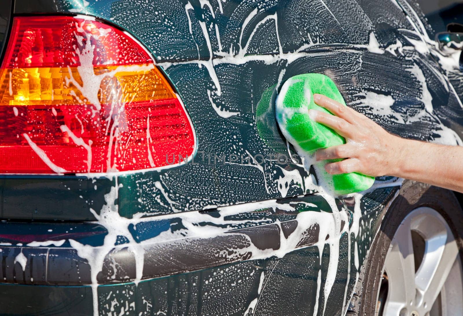 Closeup image of a hand with a soapy sponge washing a vehicle