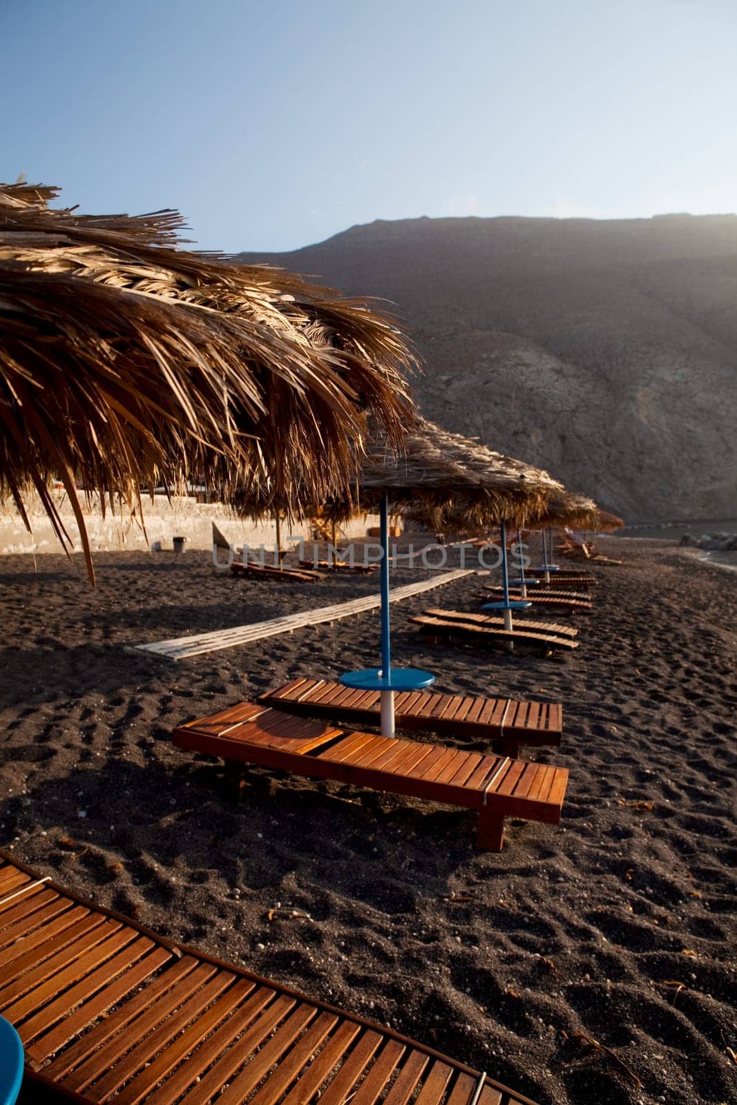 Beach umbrellas and sunbeds at sunrise in Perissa beach, Santorini, Greece
