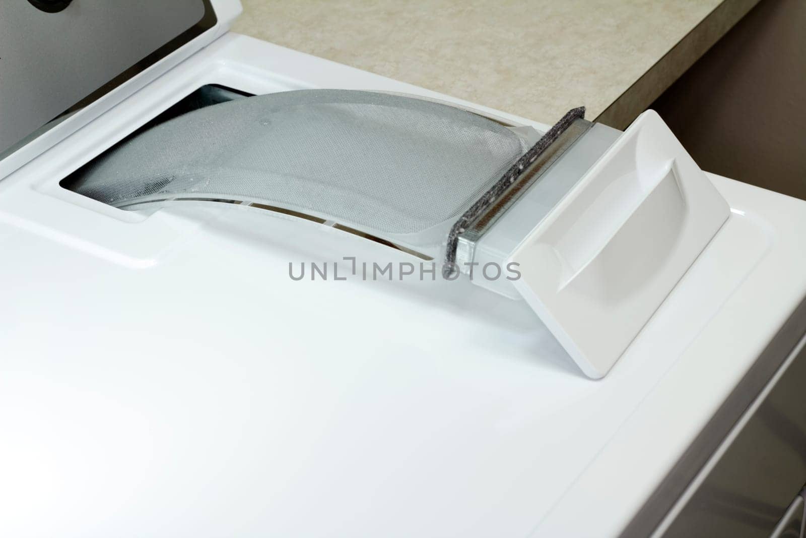 Dust collector pulled out of a white appliance that dries clothes in a laundry room.