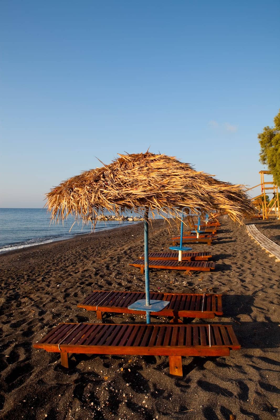 Beach umbrellas and sunbeds at sunrise in Perissa beach, Santorini, Greece