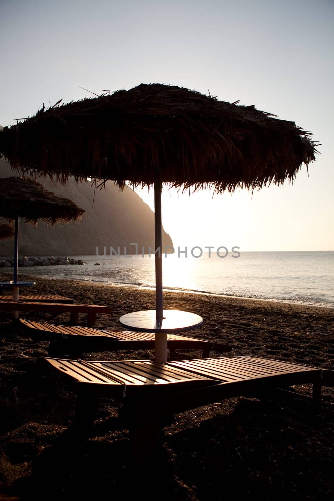 Beach umbrellas and sunbeds at sunrise in Perissa beach, Santorini, Greece