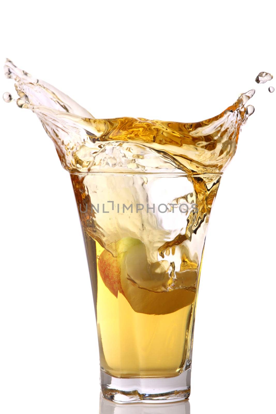 A piece of apple falls into a glass of apple juice