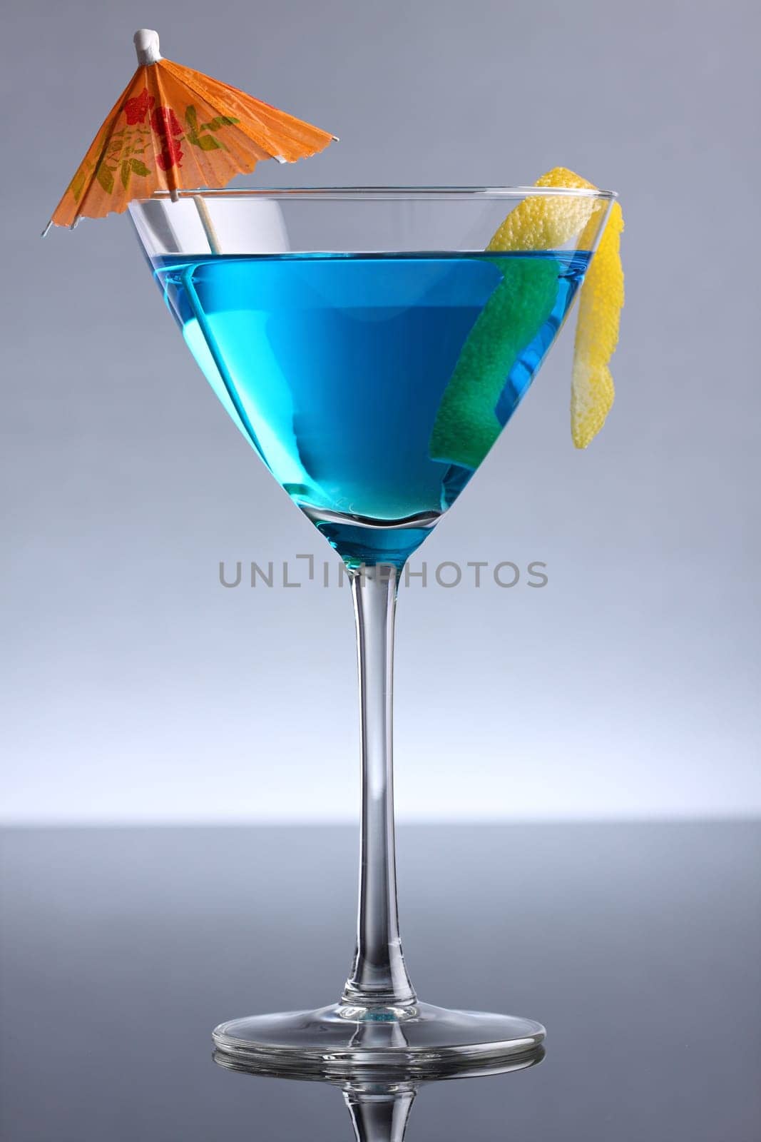 Blue cocktail with umbrella and lemon zest.