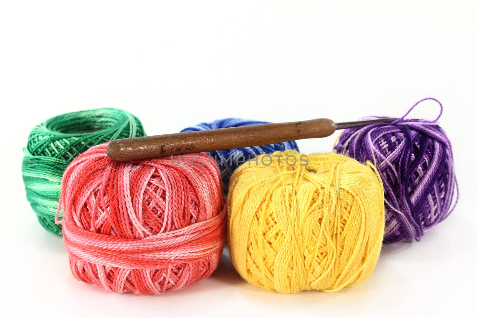 Colorful ball of wool and crochet hook against white background
