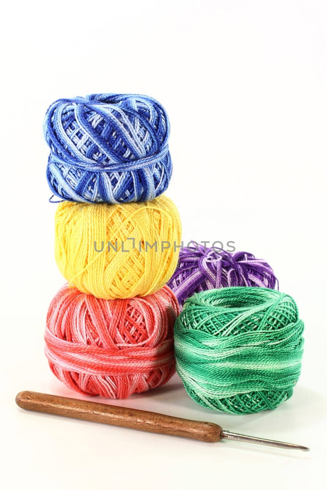 Colorful ball of wool and crochet hook against white background