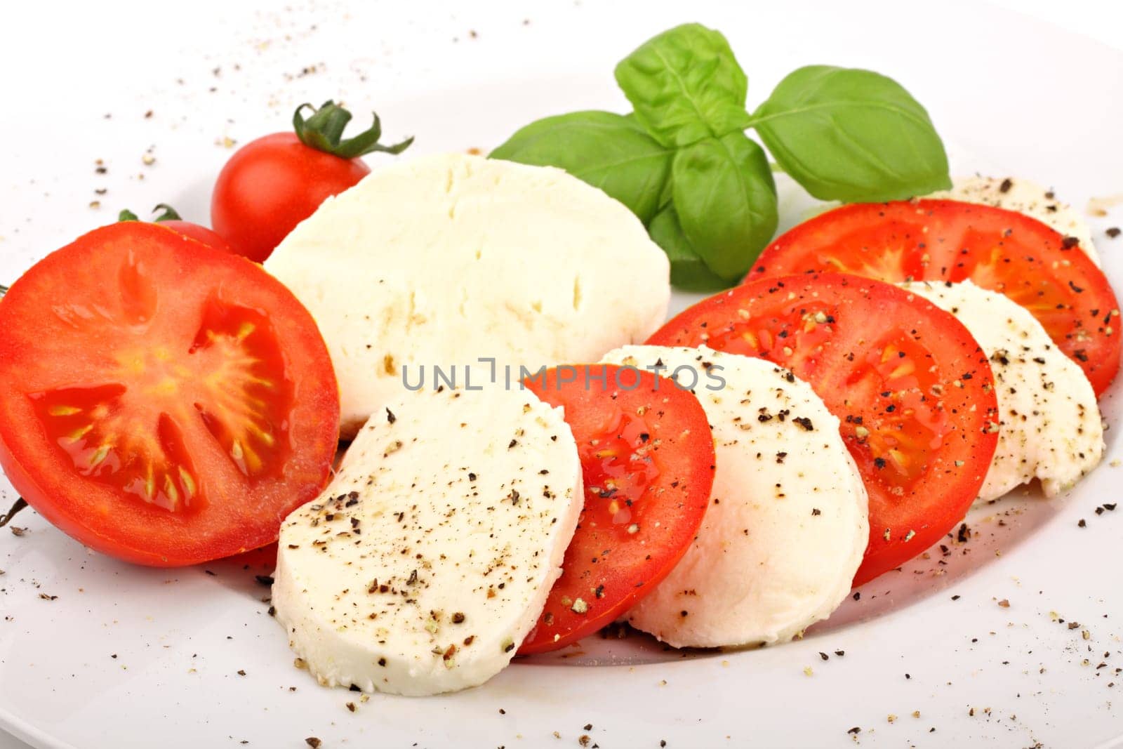 Mozzarella and tomato slices on plates with pepper and basil.