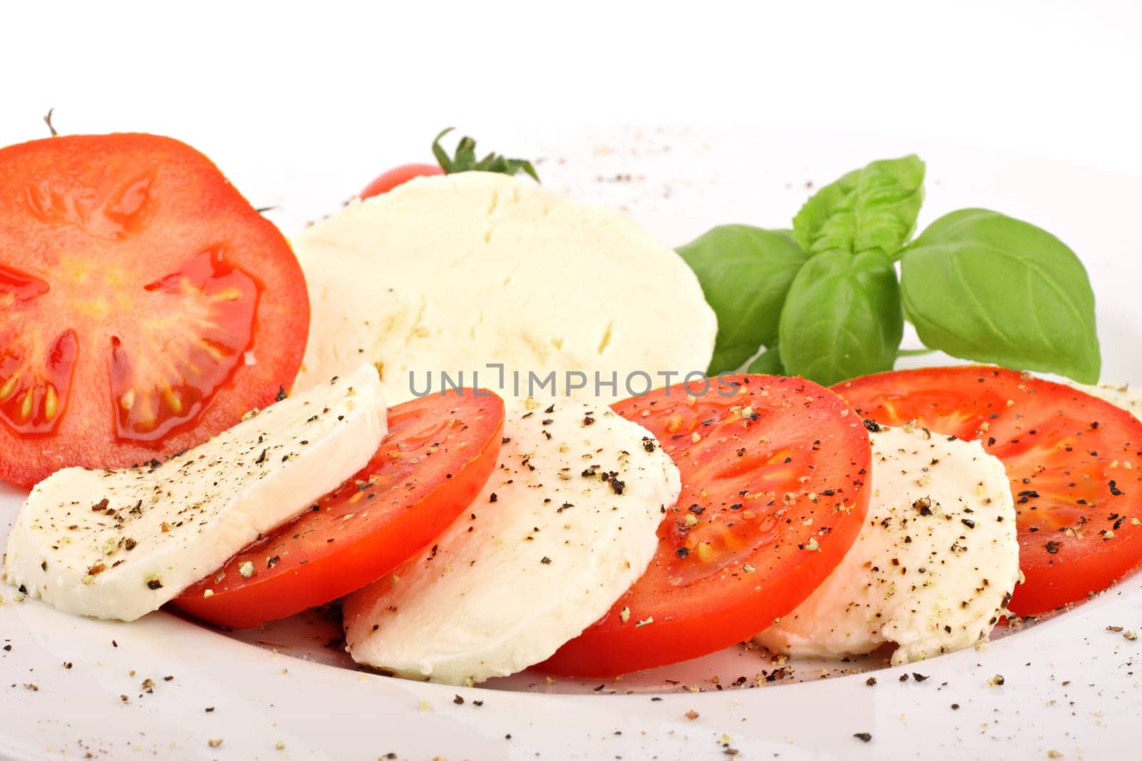 Mozzarella and tomato slices on plates with pepper and basil.