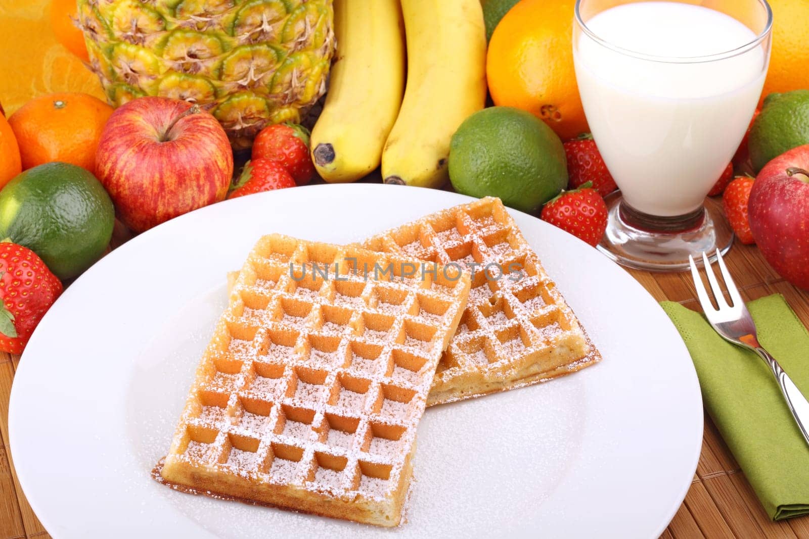 Waffle with powdered sugar on white plate in front of fruits.