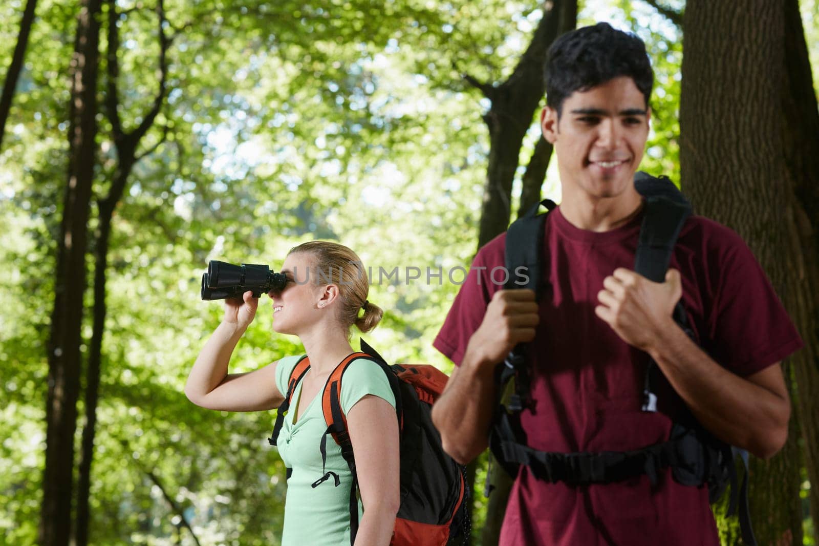 young people trekking among trees and looking at birds with binoculars. Horizontal shape, side view, waist up