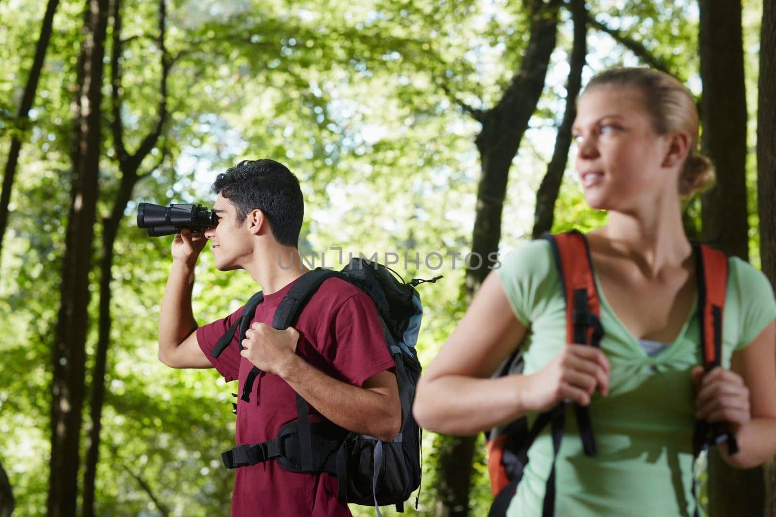 young people trekking among trees and looking at birds with binoculars. Horizontal shape, side view, waist up