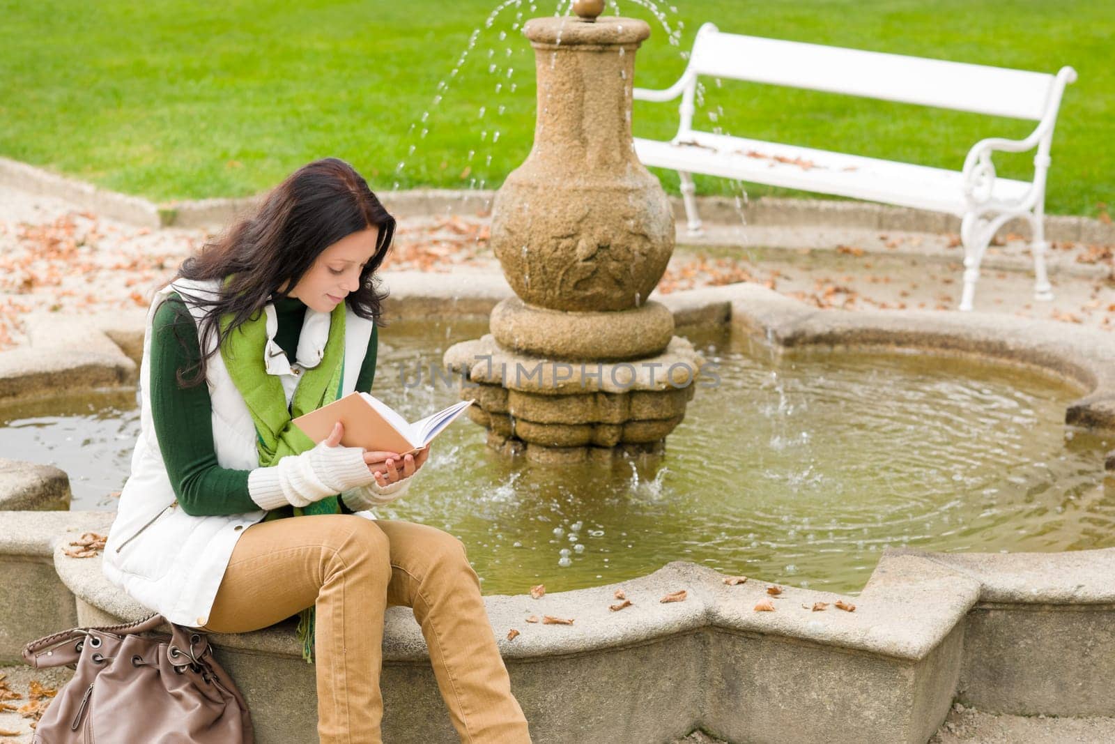 Autumn park young woman reading book sitting on fountain