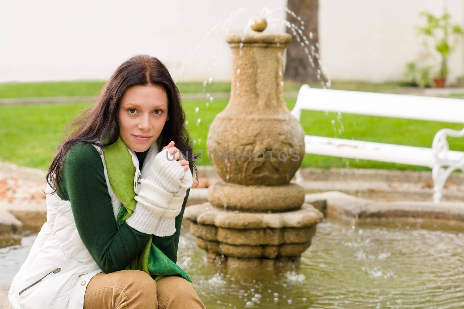 Autumn park young beautiful woman sitting on fountain cloudy day
