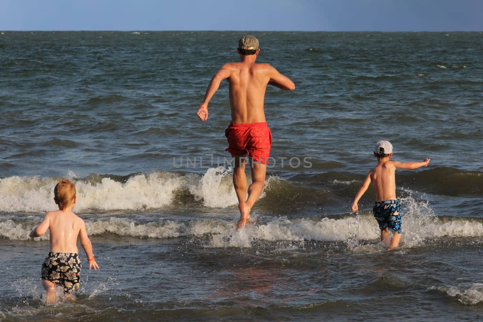 Father and his two sons running into the ocean and having fun