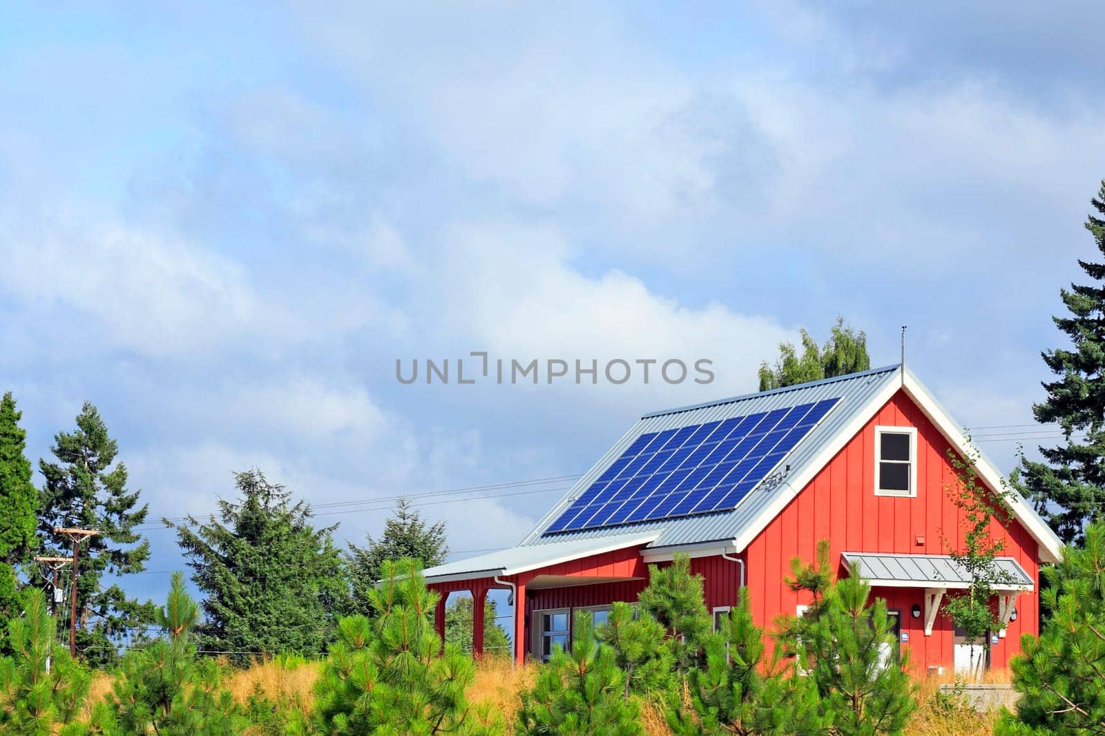 Bright red building with solar panels on the metal rooftop on a mostly sunny summer day in a public park.