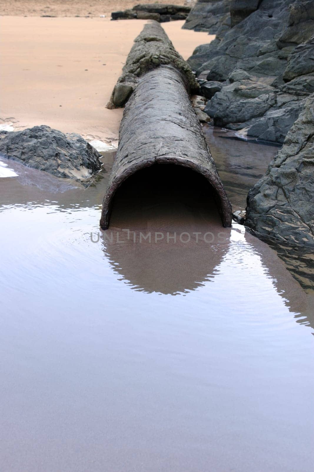 a rusty overflow pipe coming from the land to the sea