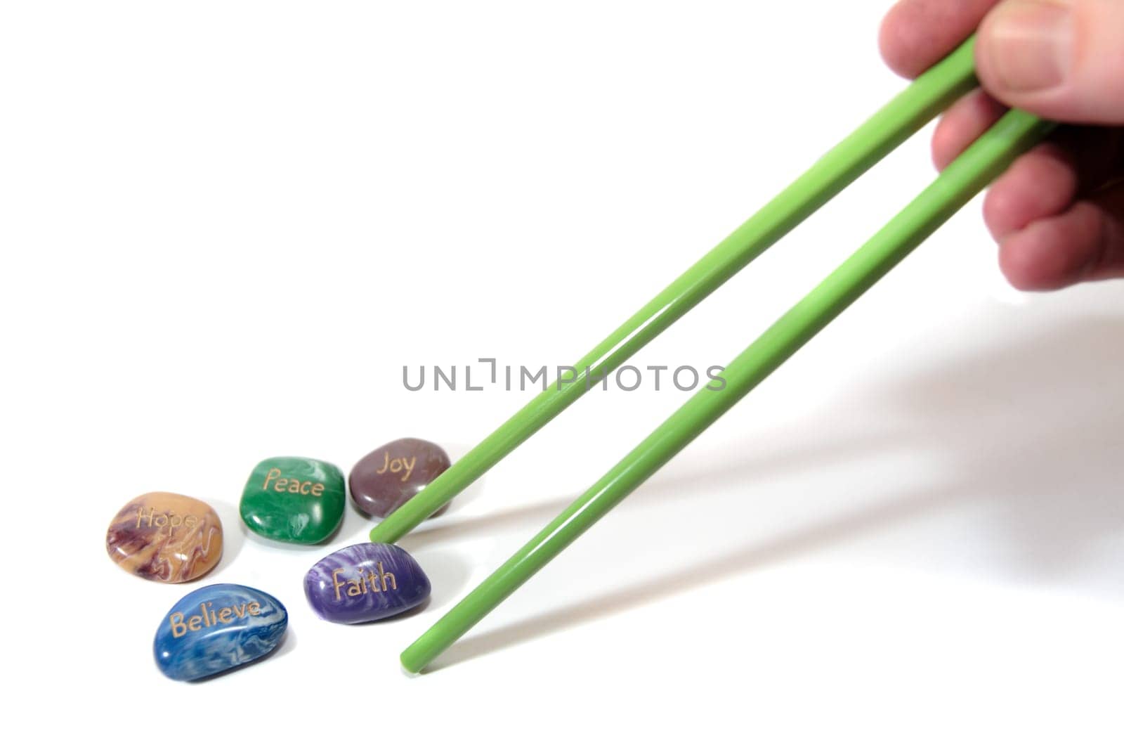 five stones inscribed hope joy peace faith and believe being picked up by chopsticks showing have belief with shadows