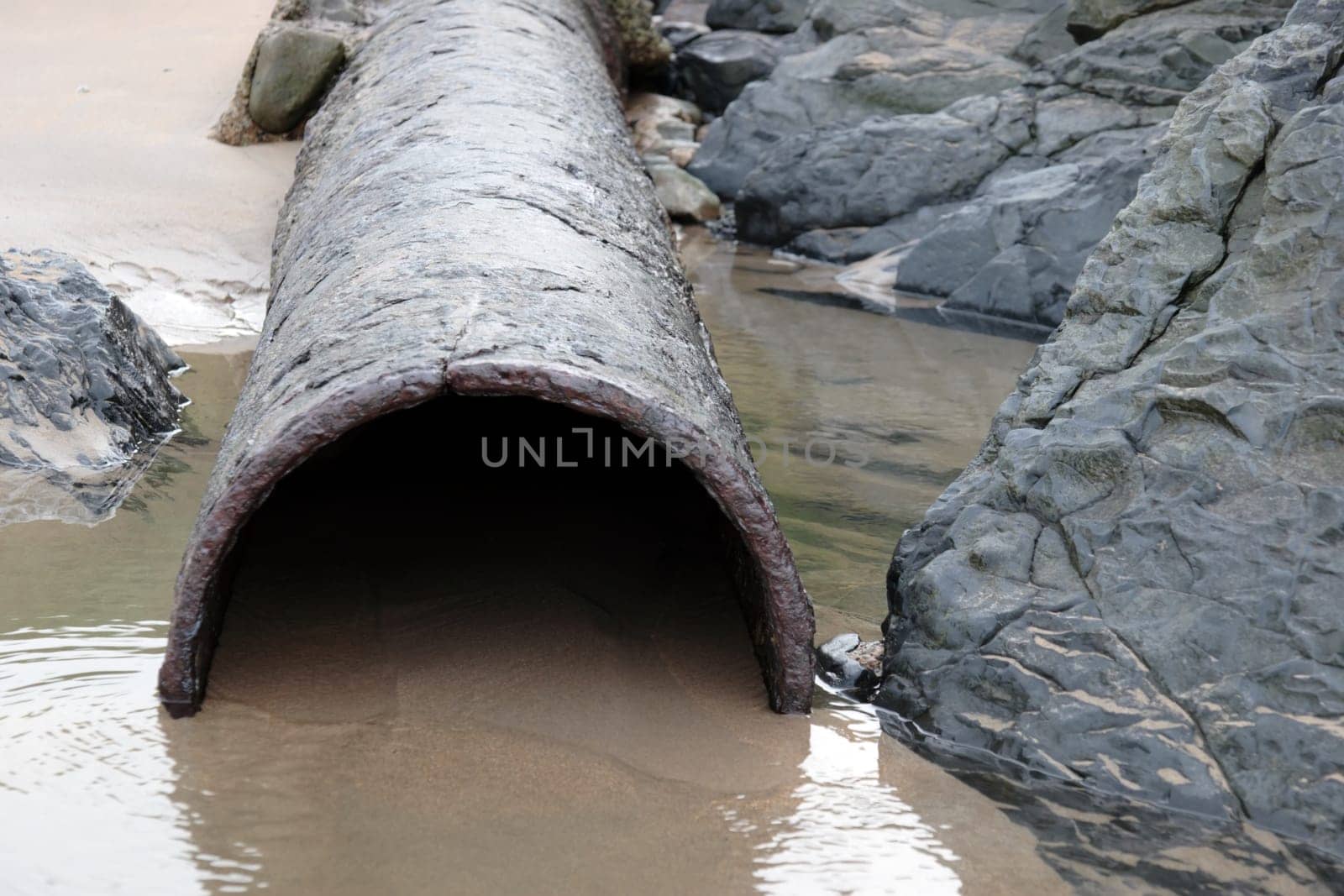 a rusty overflow pipe coming from the land to the sea